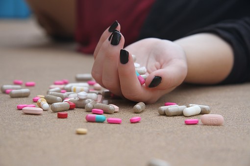 girl lying on her back, no face shown, hand full of pills that are also scattered all around her